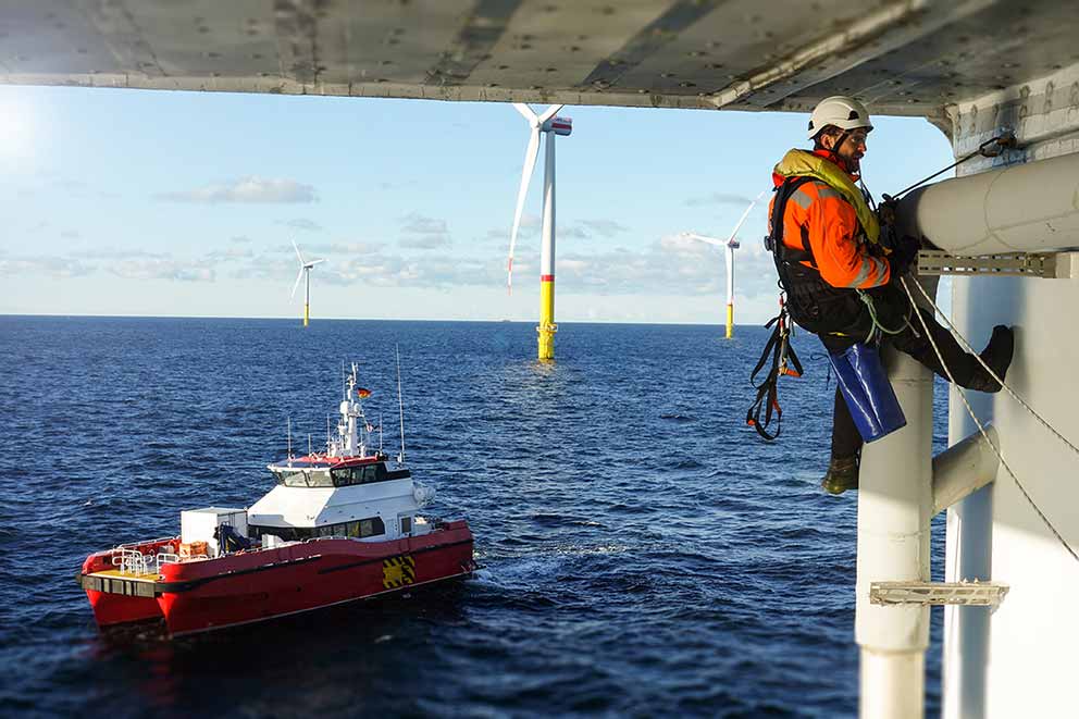 A technician repairs an offshore platform with a transfer vessel guarding in the background.
