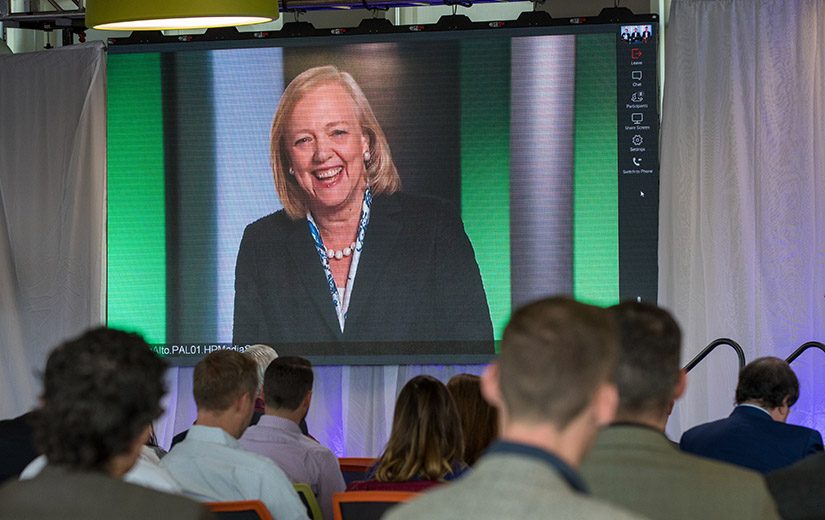 Photo of a woman's face appearing on a large monitor screen in front of a seated crowd