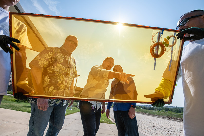 Three men watch as two others carry a large piece of glass.