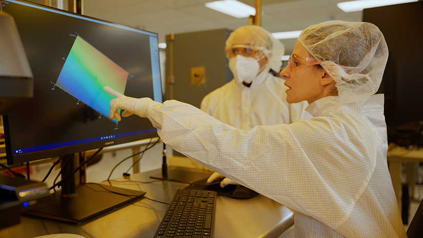 Two people in full lab gear look at a thermal image on a computer screen.