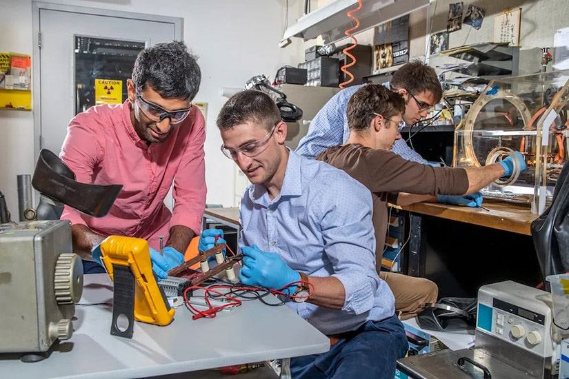 Four people work on technology in a lab, focusing on equipment and with safety glasses on. 