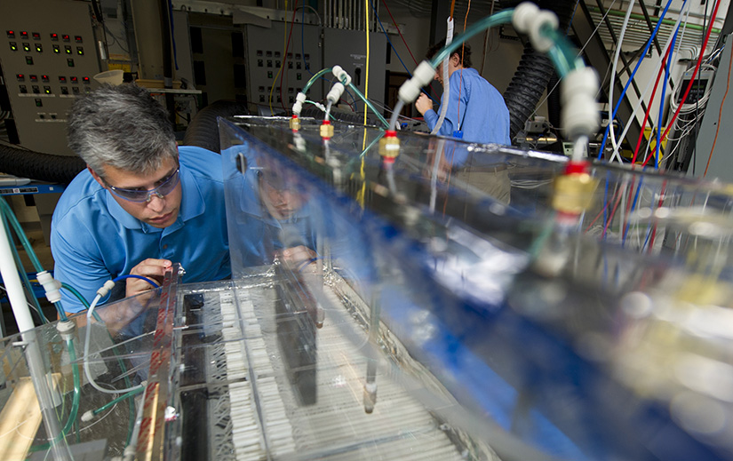 A man closely examines testing equipment with many wires and a clear box.