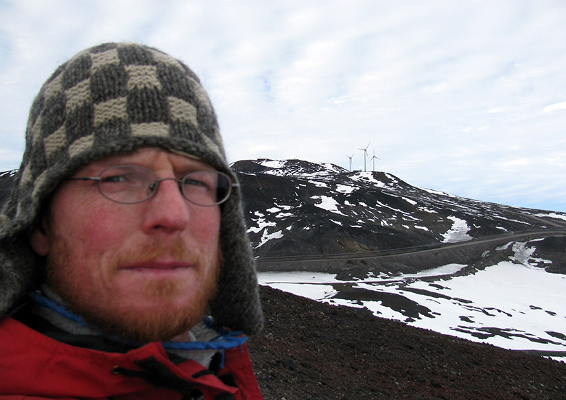 A man stands in the foreground of a photo that shows three wind turbines in the background.