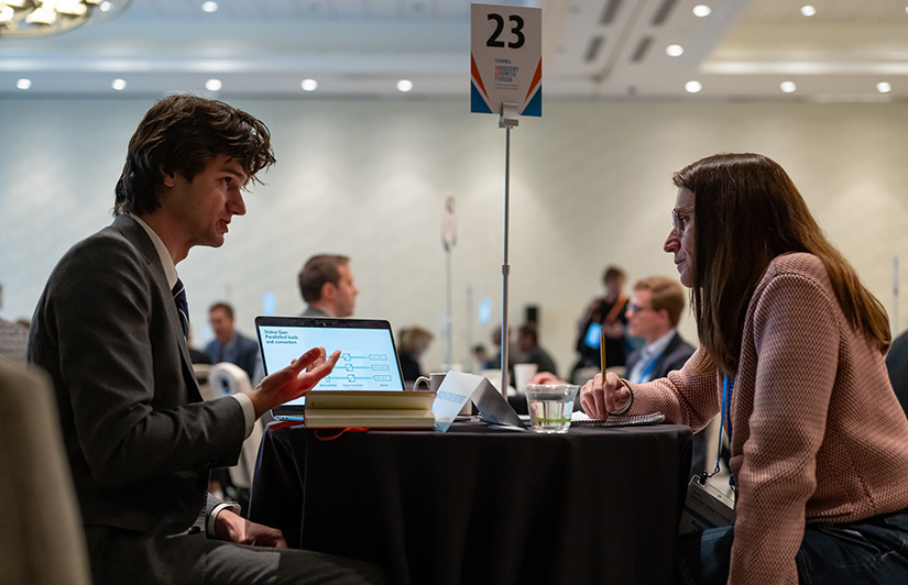 A man sits at a small table talking to a woman taking notes.