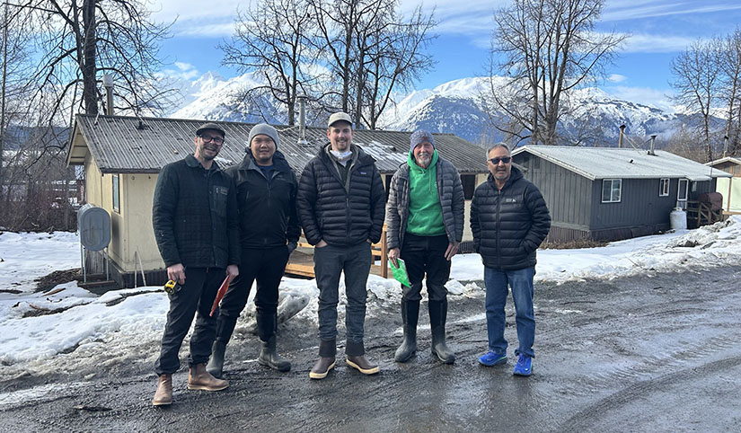 Five people stand on a road in front of a house.
