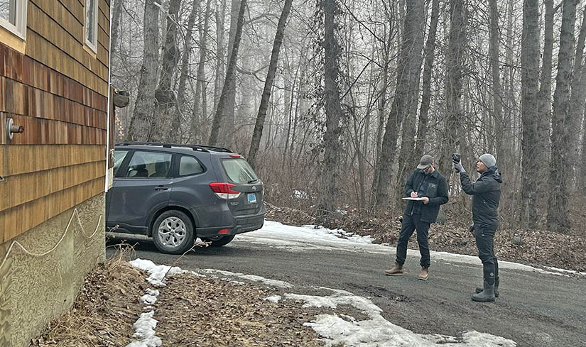 Two people assess the outside of a home.