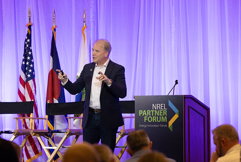 A person standing next to a podium gestures while speaking to an audience.