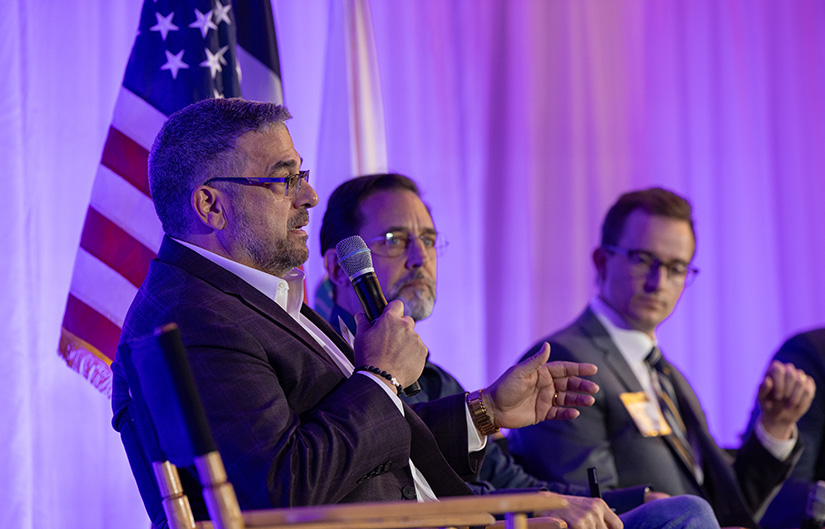 A person holding a microphone speaks on a panel.