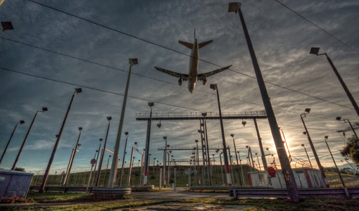 Continue reading about Photo of a large commercial airplane flying over electric infrastructure at an airport