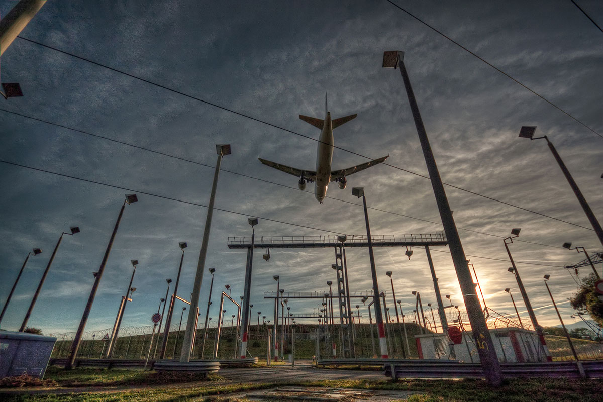Photo of a large commercial airplane flying over electric infrastructure at an airport