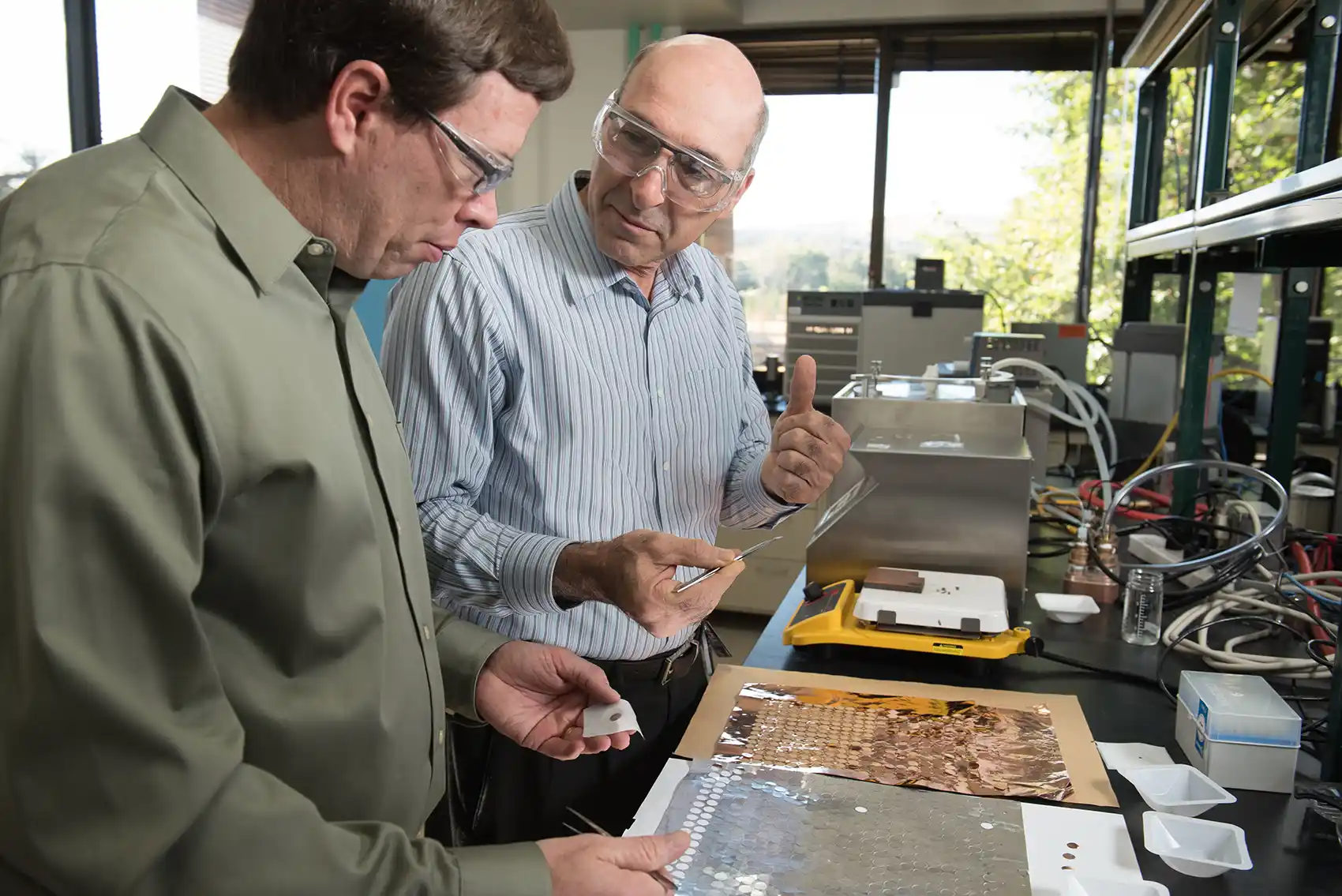 20260513-nlr-battery-innovation-awarded-nasa-invention-of-the-year-034824 Two people examine a sheet of metal discs in a lab.
