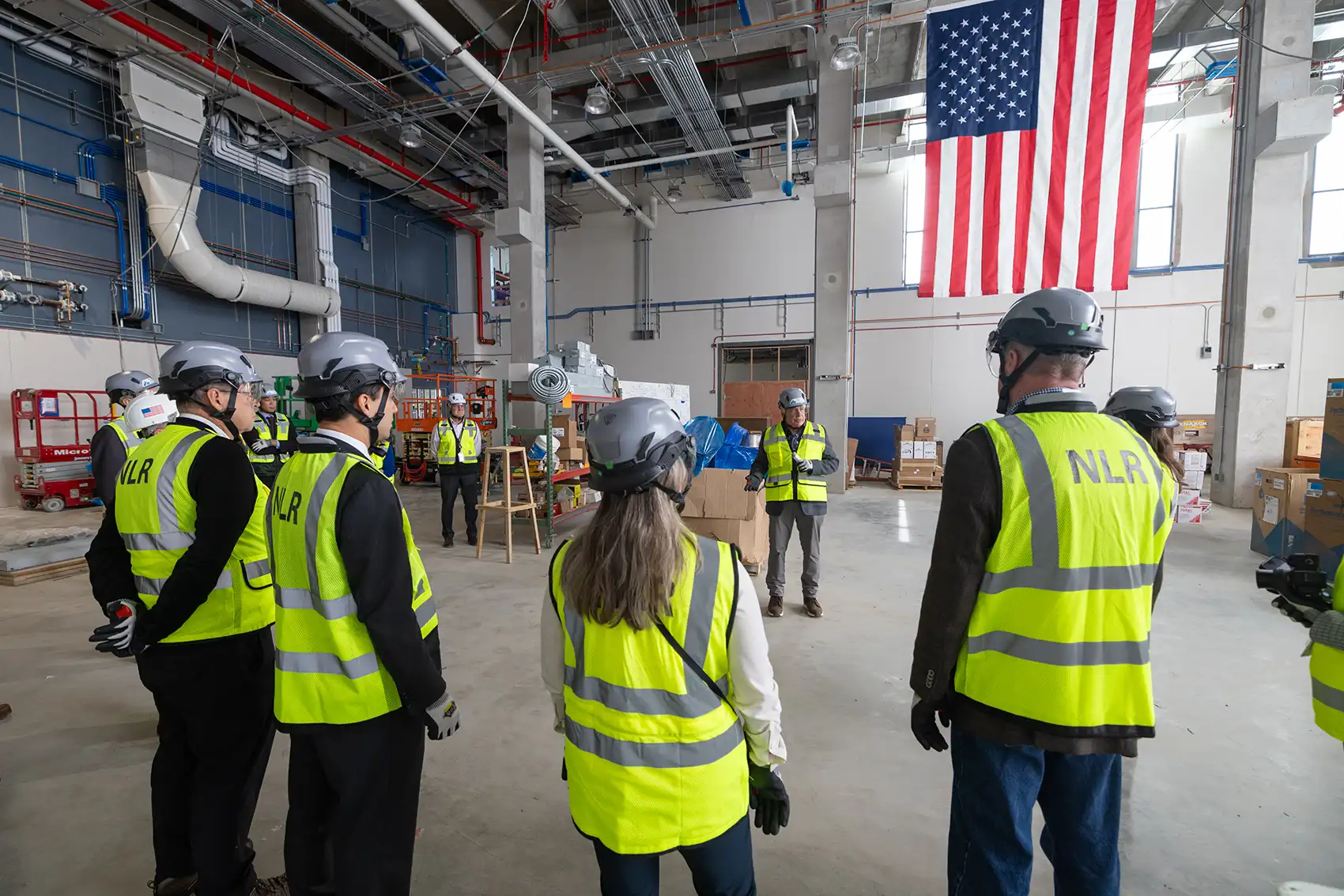 A group of people in hard hats and safety vests stand in a warehouse.