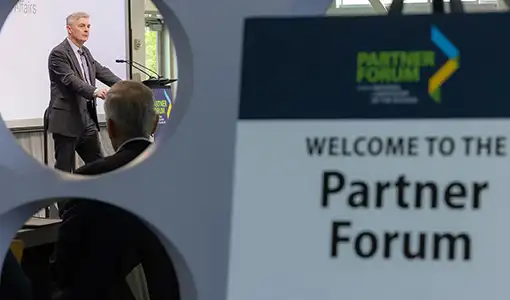 Continue reading about A person speaking at a podium with a sign with the text Welcome to the Partner Forum in the foreground.