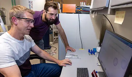 Continue reading about Two people in safety glasses look at a computer monitor.