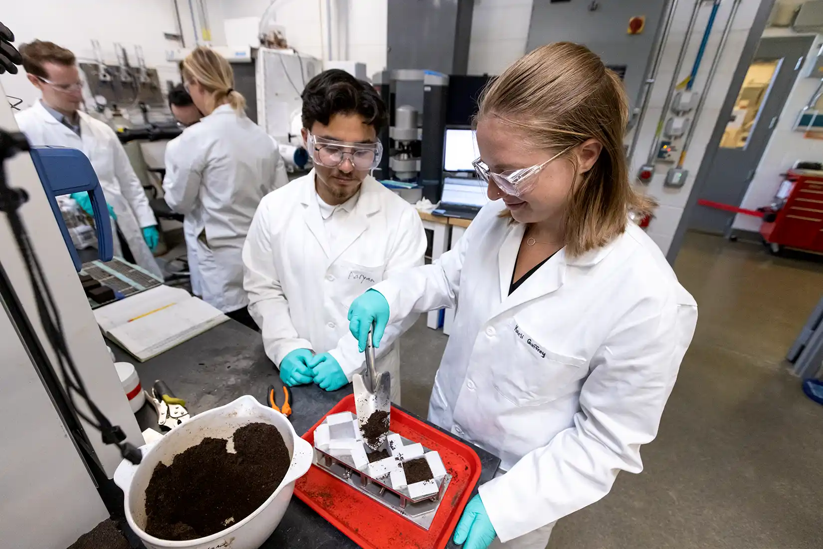 Two people in lab coats and safety glasses work in a laboratory.