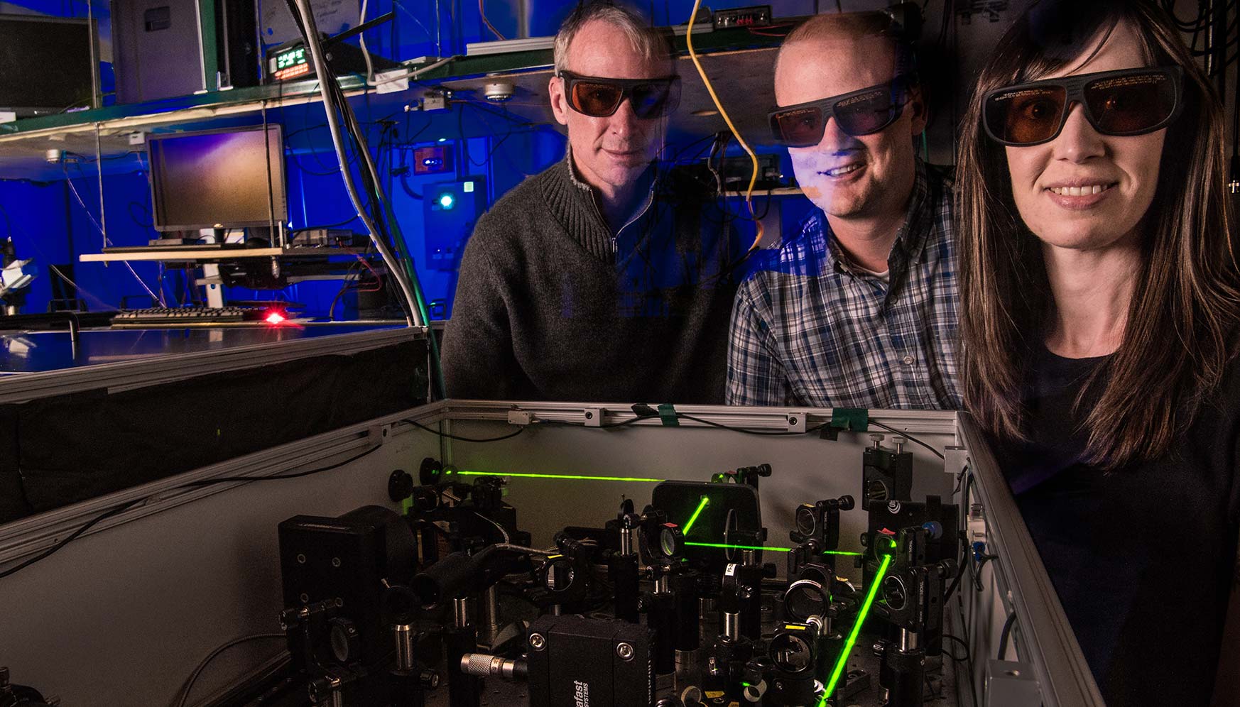 Two men and one woman wearing dark glasses stand next to a laser.