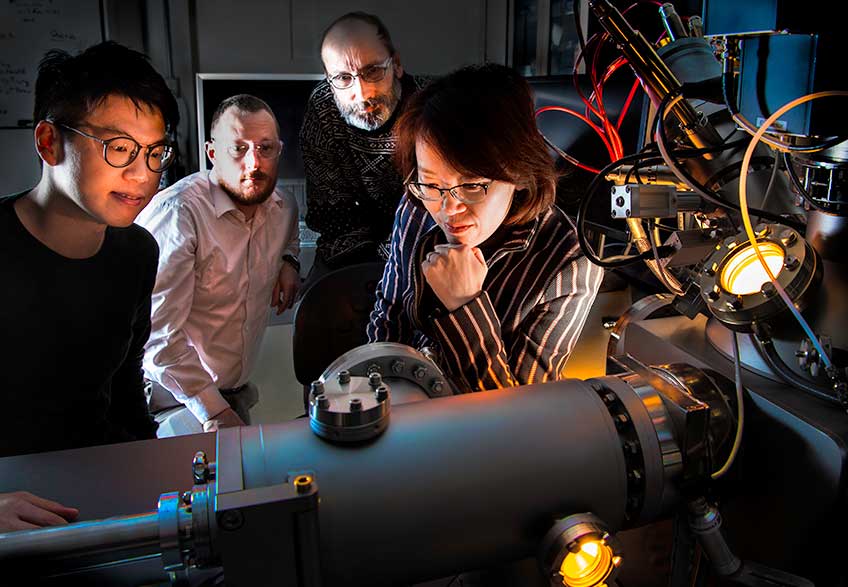 Three men and a woman examine a piece of laboratory equipment.