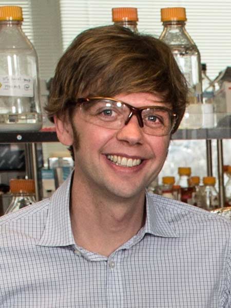 A man stands in front of a shelf of glass bottles in a laboratory.