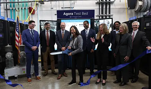 Continue reading about Eight people smile as a person cuts a ribbon with giant scissors.