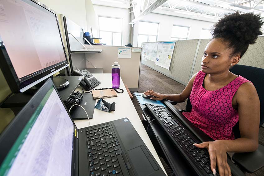 A woman sits in a cubical staring at a computer.