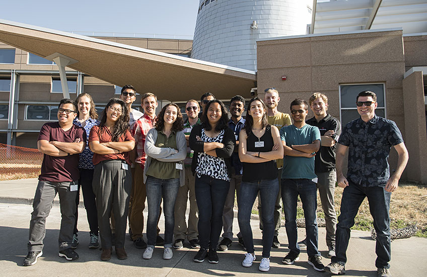 15 students pose as a group in front of one of NREL’s lab buildings.