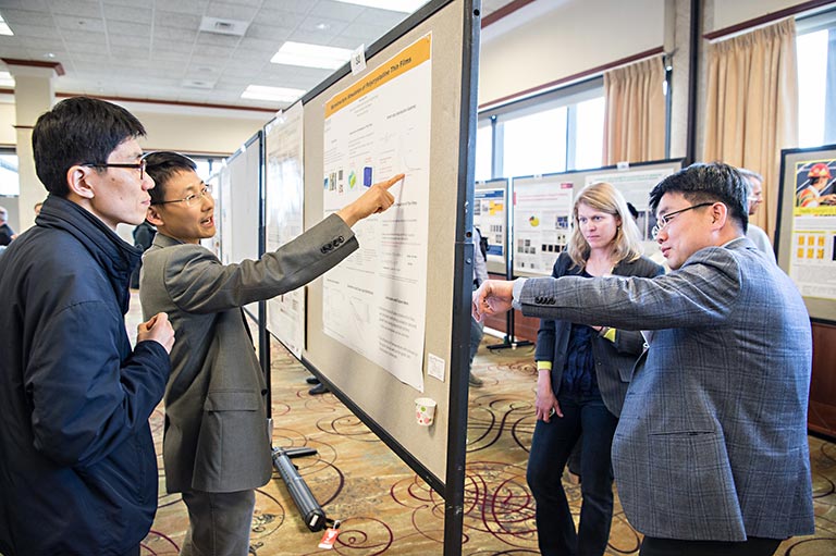 4 people consult two scientific posters in a large conference room.