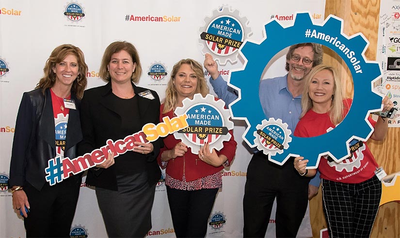 A group of five people stand in front of a wall holding photo props