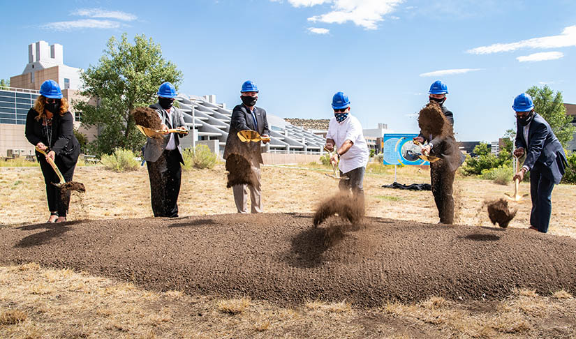 Six people outside wearing hard hats use shovels to break ground on NREL campus