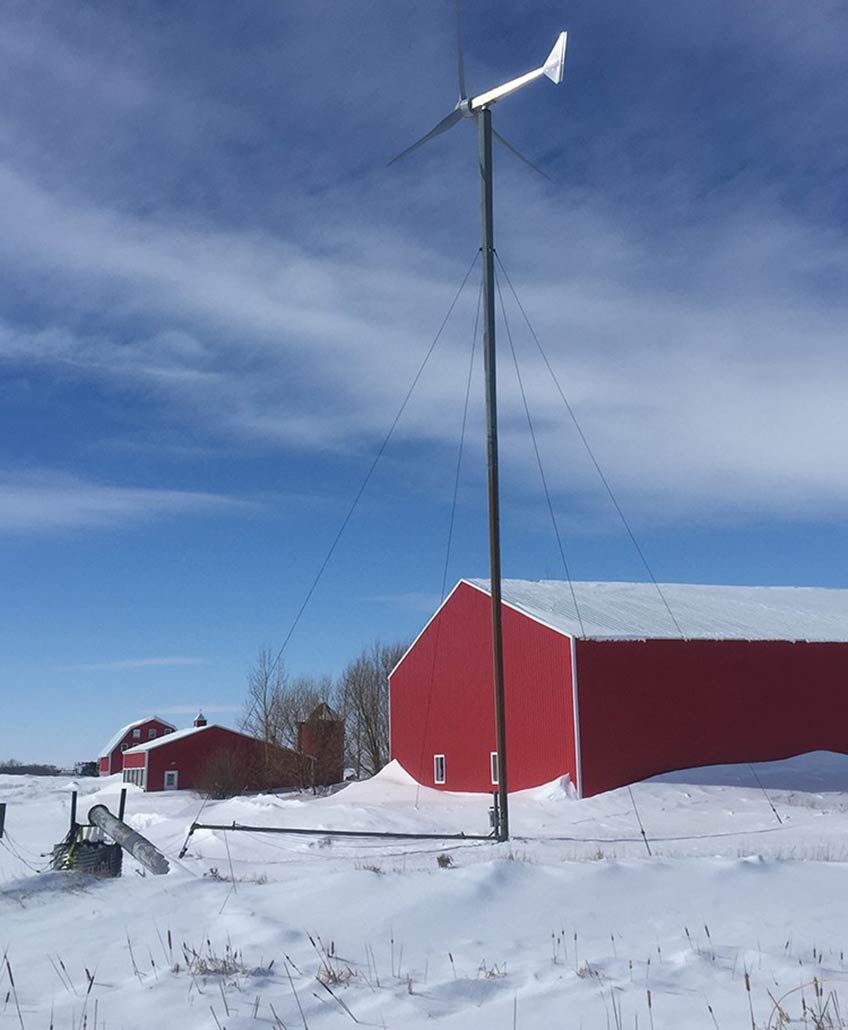 A small wind turbine next to a house in winter.
