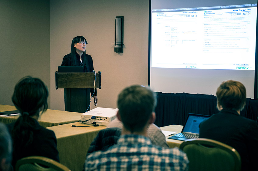 Photo of people in a meeting room with one standing at a podium.