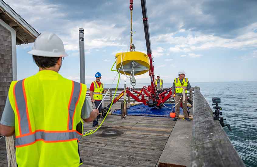 Researchers use a crane to lift a yellow buoy float into the water.