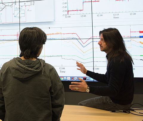 Photo of two people talking in front of a large data screen