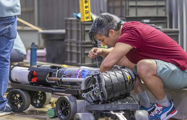 A person crouches over a device on wheels.