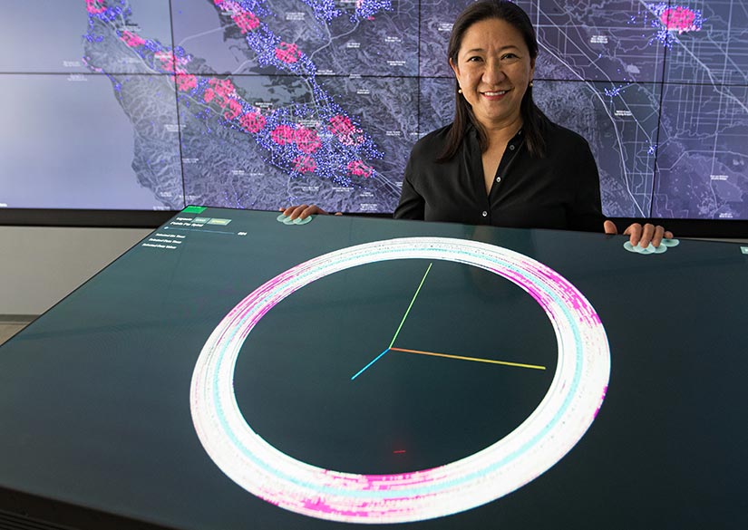 A woman stands in front of a map projection with touch screen in front of her.