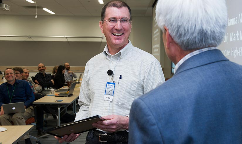 A man holding an award is smiling at another man.