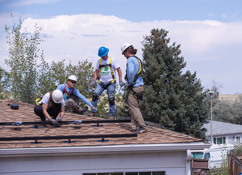 A group of people installing solar panels on the roof of a home.