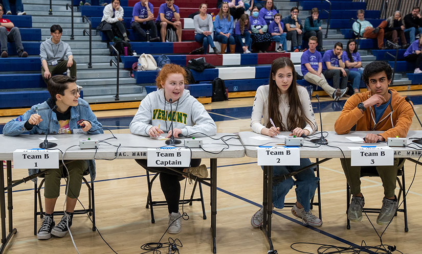 Students sitting at a table with an audience in the background.