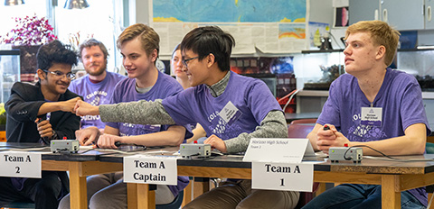 Two students fist bump across a table.