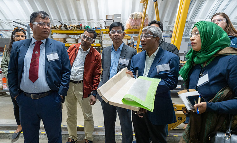 A group of nine people wear safety goggles as one man bends a flexible material.