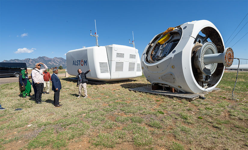 he group of representatives stands to listen to a researcher pointing at a large turbine engine in the grass.