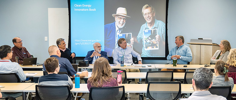 Panelists sit in front of a slideshow presentation.