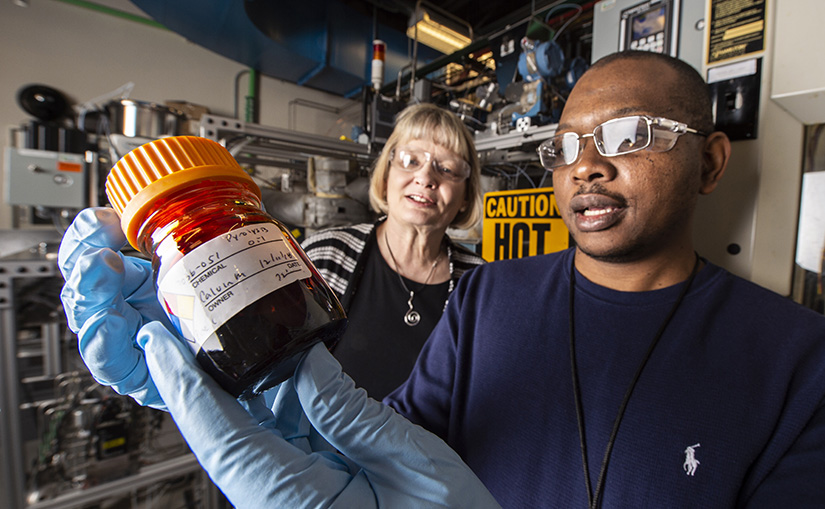 Two scientists examine a container of bio-oil in a lab.
