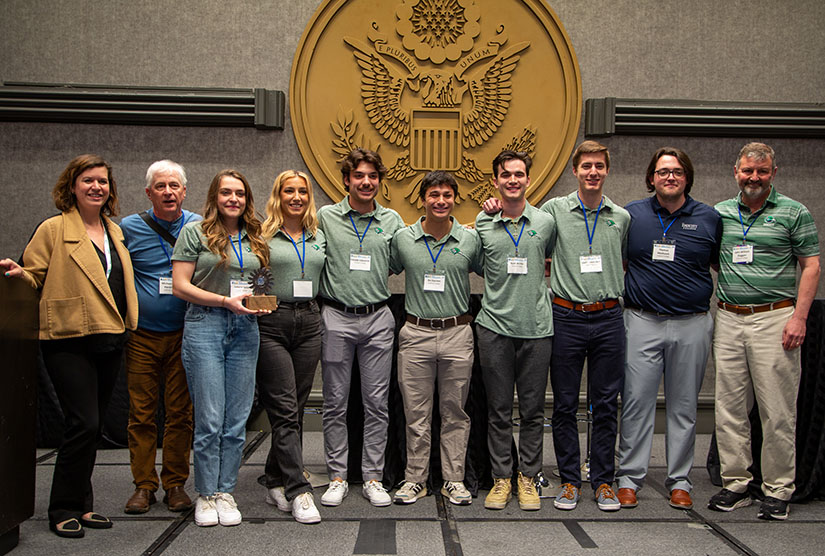 A group of students  standing in front of the U.S. seal in matching shirts and name tags.