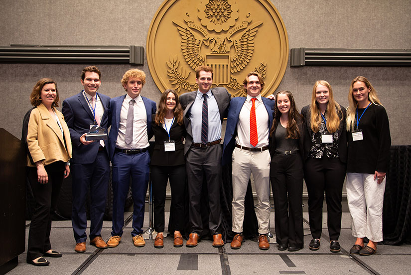A group of students standing in front of the U.S. seal in business attire.