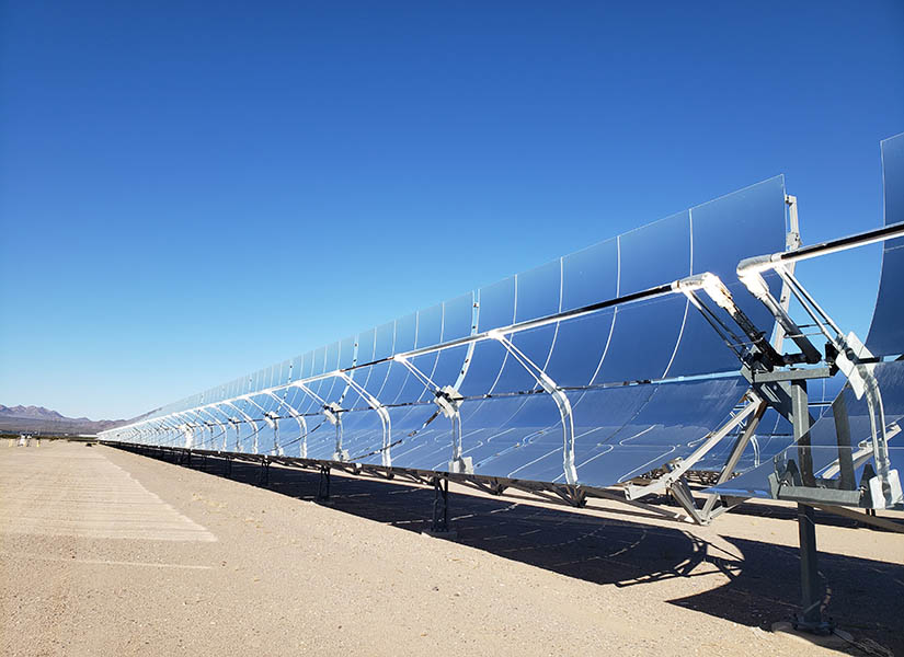 Curved, mirrored panels reflecting sunlight in a desert with mountains in the background