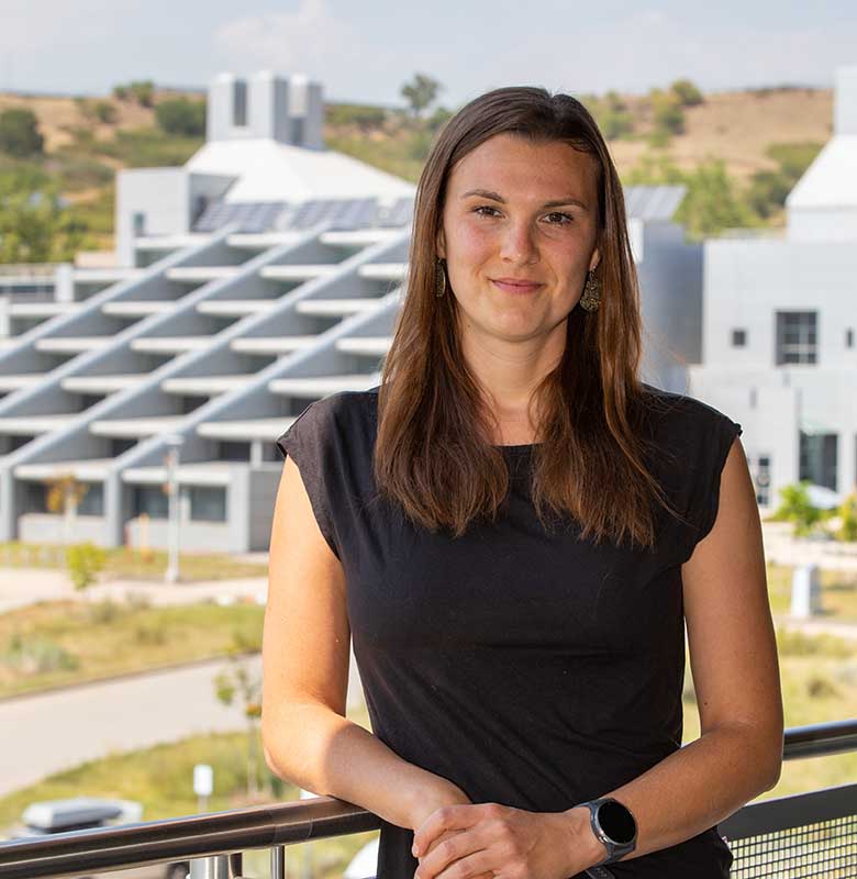Ulrike Egerer standing on a balcony in front of hills and buildings.