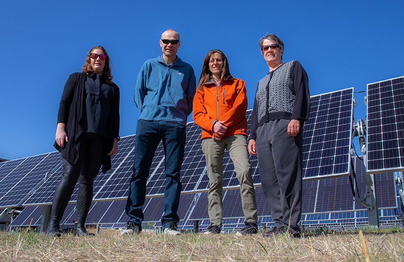 Three women and a man stand in front of a PV array.