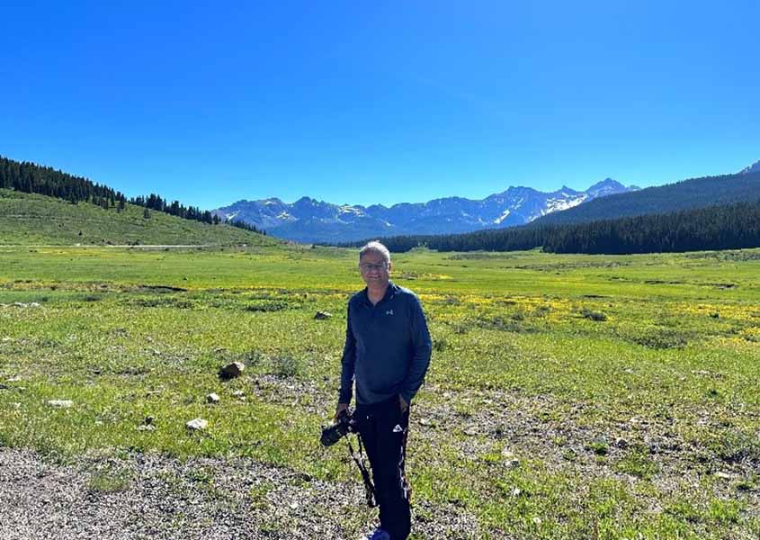 Abhishek Roy standing on a trail in a field with trees and mountains in the distance