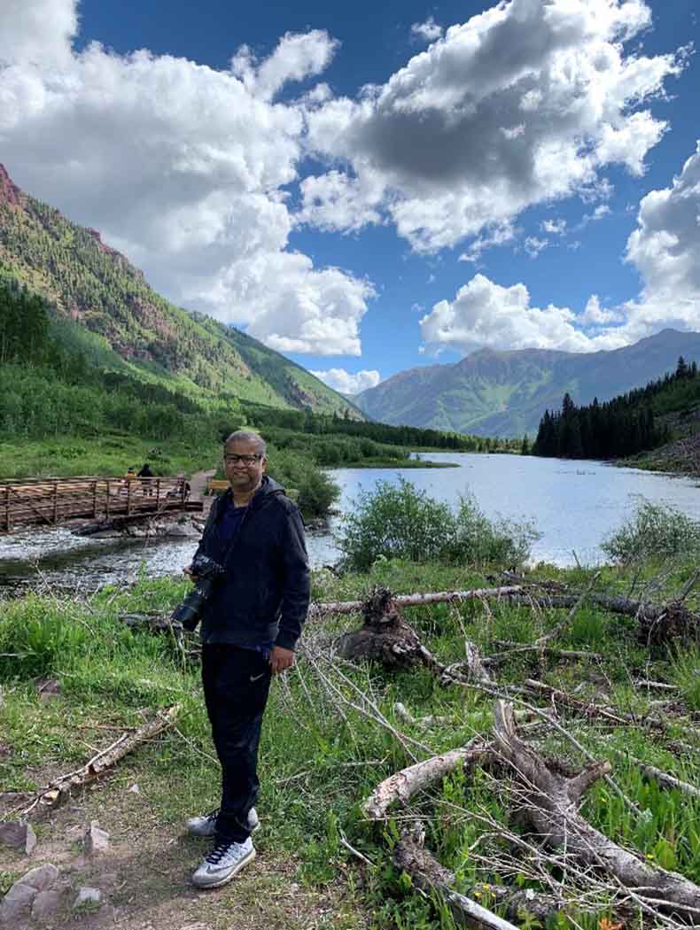 Roy standing on a trail in a mountain valley near a body of water and a wooden bridge