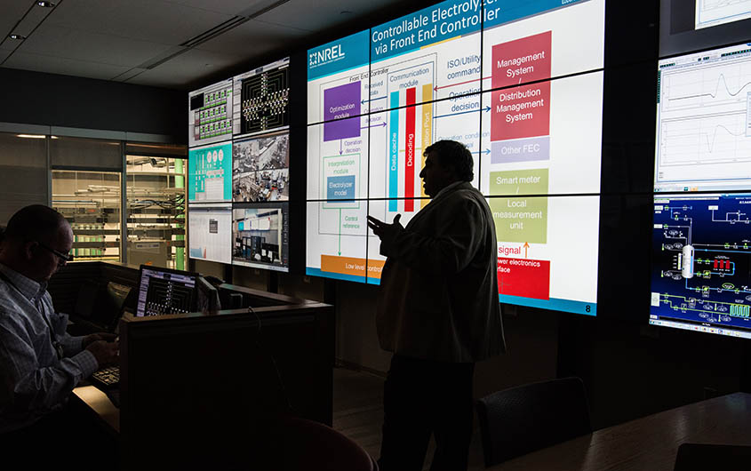 Rob Hovsapian standing in front of a bright screen while presenting to an audience in a darkly lit room